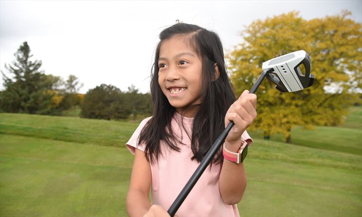 Young female golfer on the greens holding a golf club and smiling