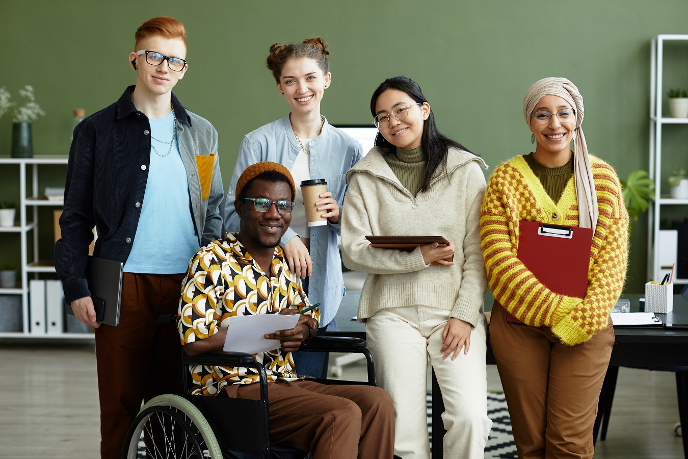 Diverse students looking at camera with cheerful smiles while posing in office